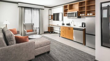 Une chambre d’hôtel moderne équipée d’un canapé, d’un bureau, d’un coin cuisine et d’une télévision.