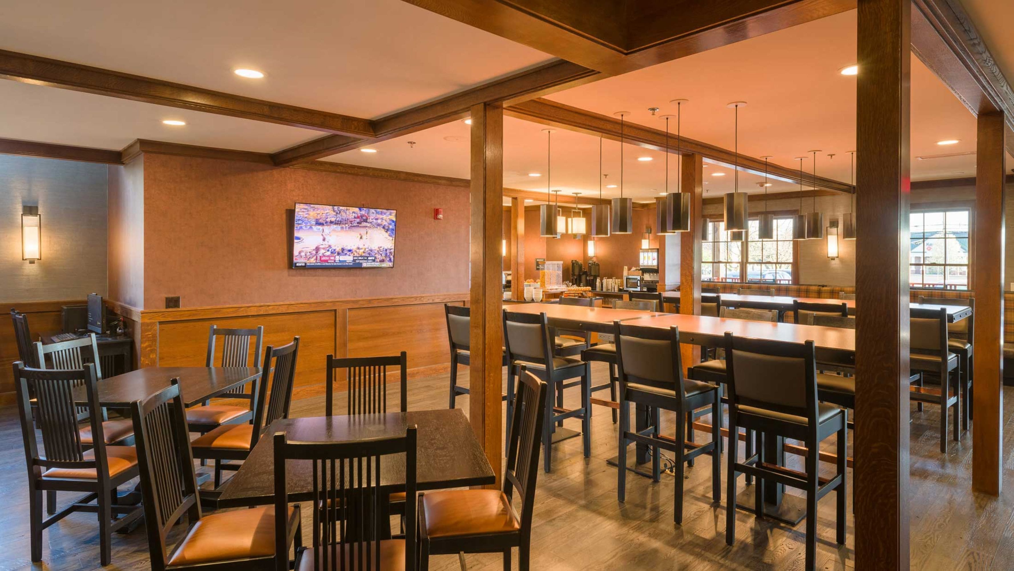 A restaurant with wooden furniture, a TV on the wall, and a kitchen area.
