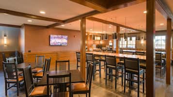 A restaurant with wooden furniture, a TV on the wall, and a kitchen area.