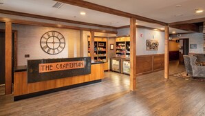 A reception area with a wooden reception desk labeled "The Craftman," a large wall clock, and a refrigerator stocked with beverages.