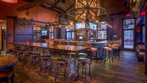 A bar area with wooden floors, metal bar stools, and hanging pendant lights.