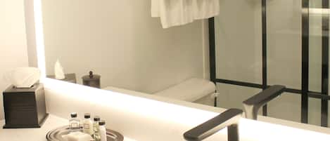 A modern bathroom with a large mirror, a white sink, and a glass-enclosed shower.