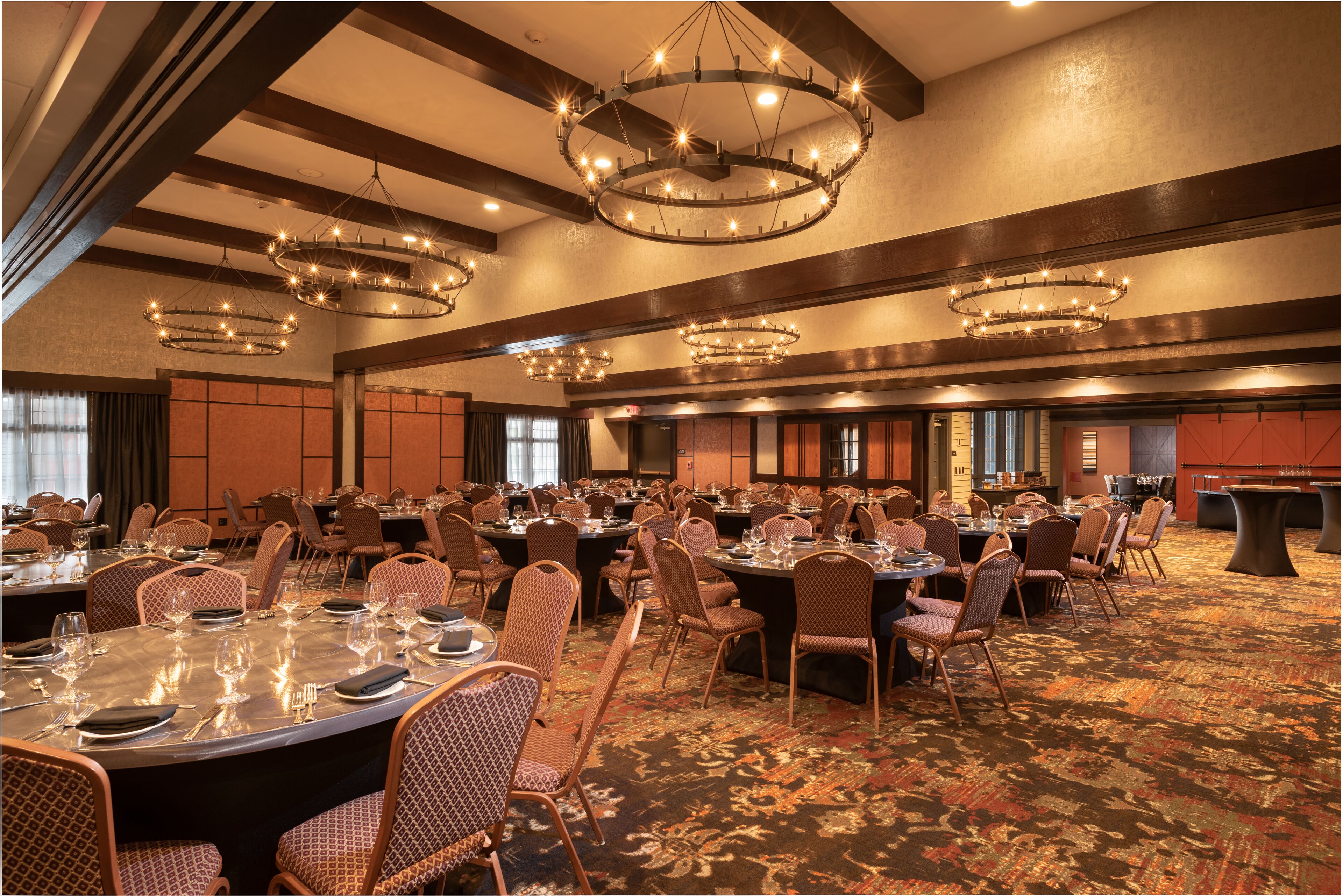 A spacious banquet hall with multiple round tables set for dining, surrounded by upholstered chairs.