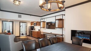 A modern hotel room with a dining area, kitchenette, and a TV mounted on the wall.