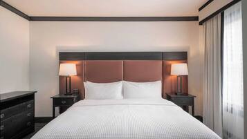 Habitación de hotel con una cama grande, dos mesitas de noche con lámparas, un aparador y una ventana con cortinas.