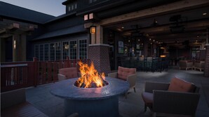 An outdoor patio with a circular fire pit, wicker furniture, and a brick wall.