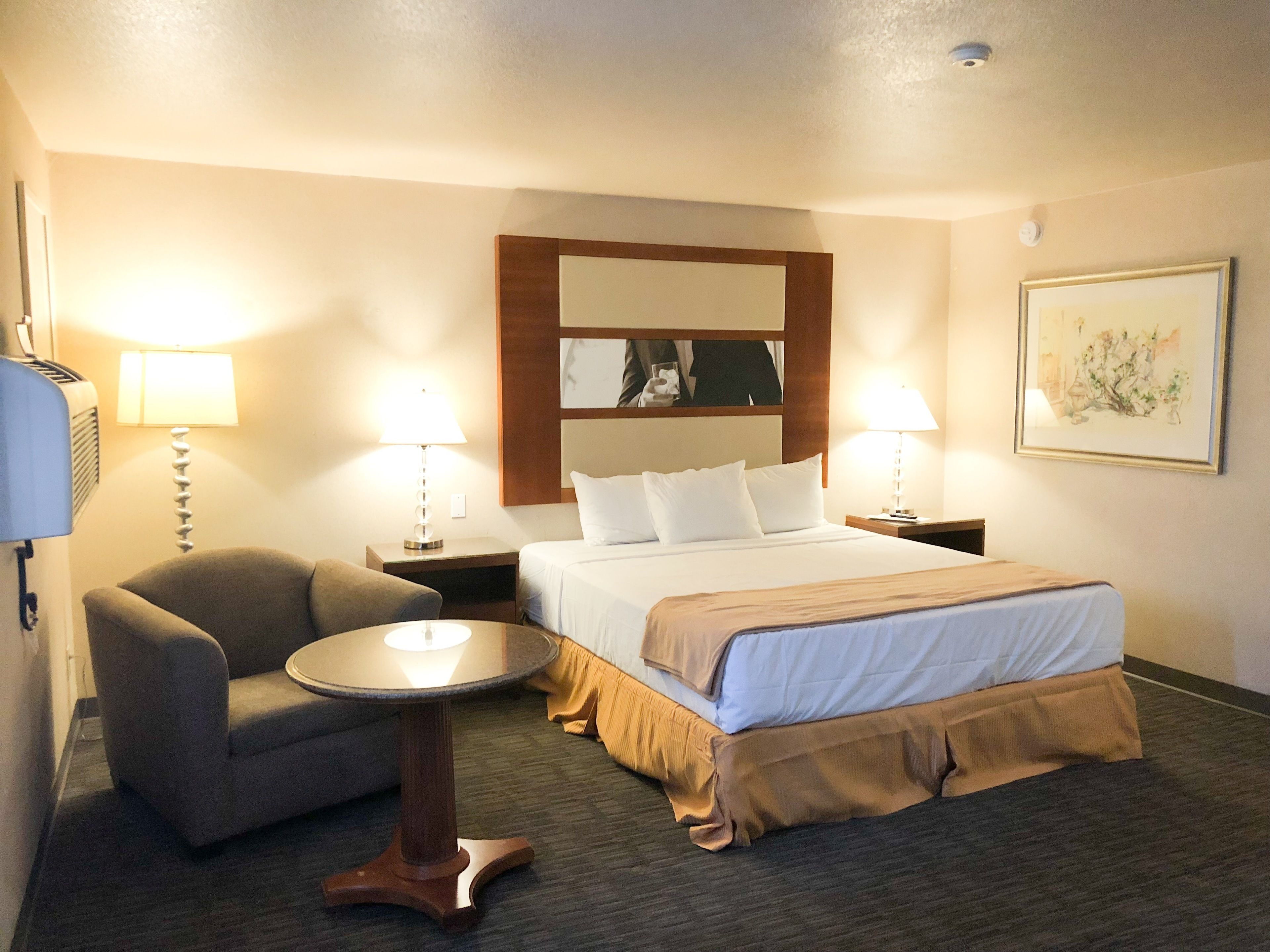 Een hotelkamer met een bed, een stoel, een klein tafeltje en twee bedlampjes.