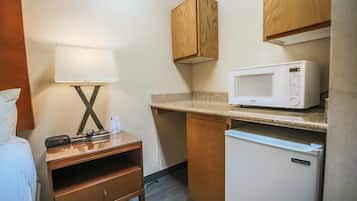 Une petite cuisine équipée comprenant un four à micro-ondes, un petit réfrigérateur, un meuble en bois et une table de chevet avec une lampe.