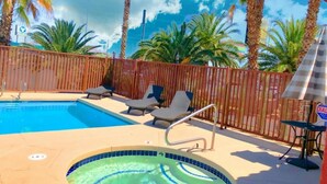 Une piscine dotée de chaises longues et d’un jacuzzi, entourée de palmiers et d’une clôture en bois.