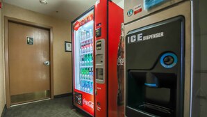 Un couloir avec un distributeur automatique de Coca-Cola, un distributeur de glaçons et une porte portant l’inscription « Hommes ».