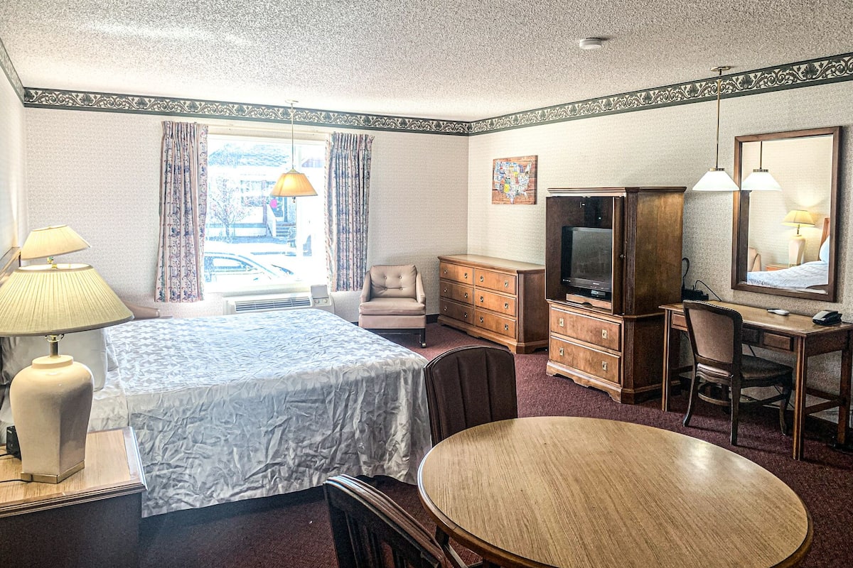Ein Hotelzimmer mit Bett, Schreibtisch, Stuhl, Fernseher und einem fensterbepflegten Fenster.