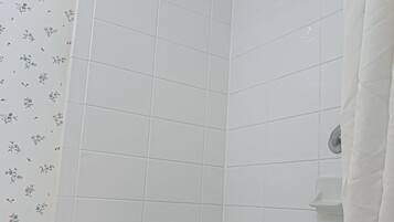 Un baño con azulejos blancos, una cortina de ducha y una bañera con una toalla blanca.