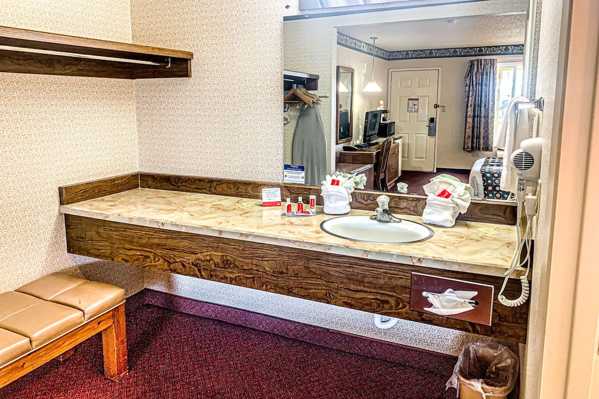Ein Badezimmer mit Marmorplatte, Waschbecken, Spiegel, Sitzbank und Mülleimer.