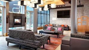 A modern lobby with a fireplace, seating area, and large windows. - Aloft by Marriott New York LaGuardia Airport (East Elmhurst)