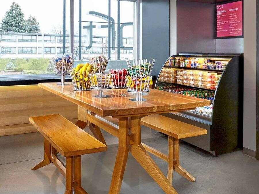 Een houten tafel met banken in een modern interieur, nabij een koelvitrine met drankjes.