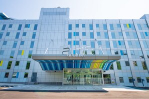 A modern hotel with a glass entrance and a blue and yellow awning. - Aloft by Marriott New York LaGuardia Airport (East Elmhurst)