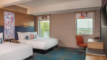 A hotel room with two beds, a desk, a chair, and a large window offering a view of the city.