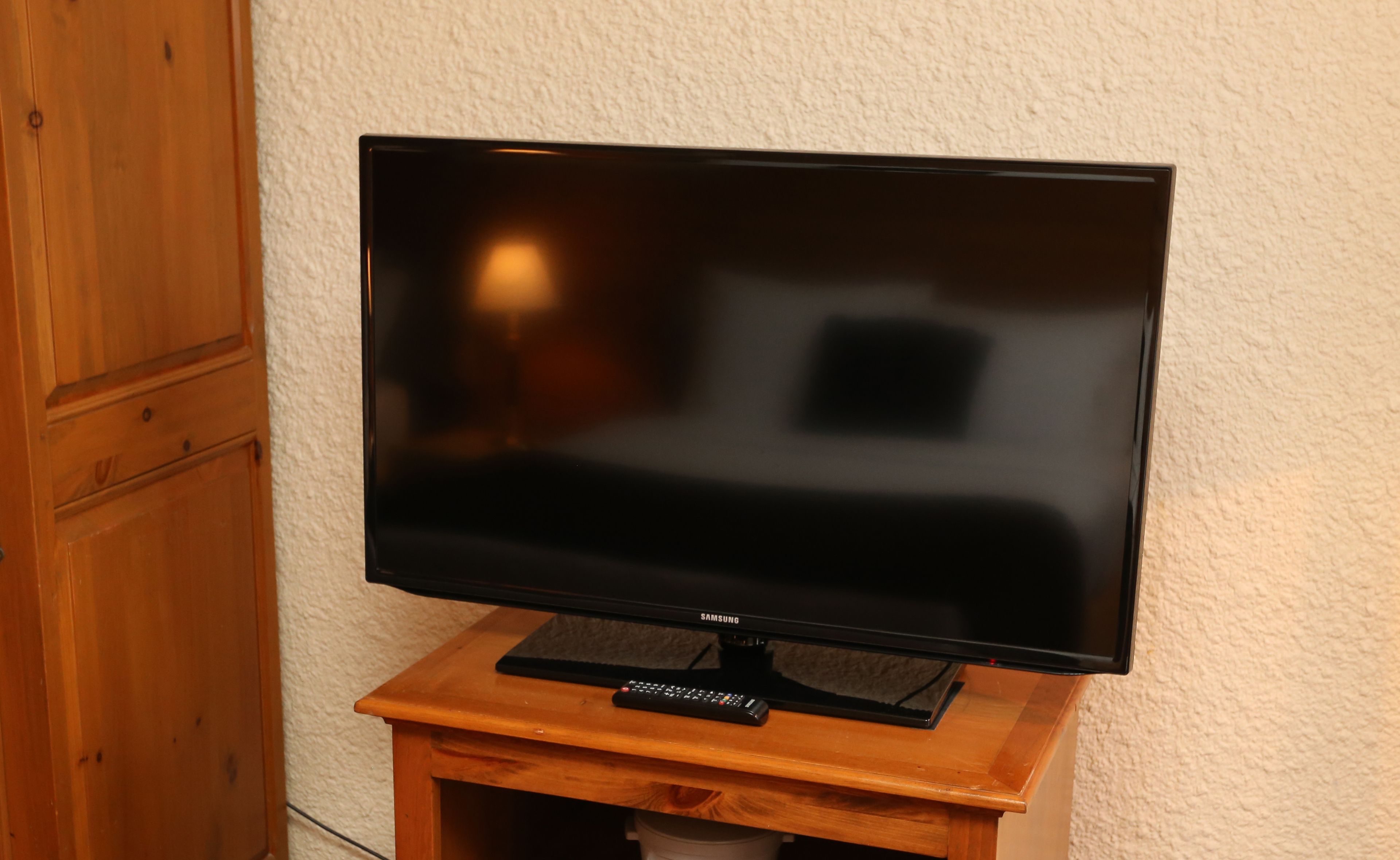 A flat-screen TV on a wooden stand with a remote control.