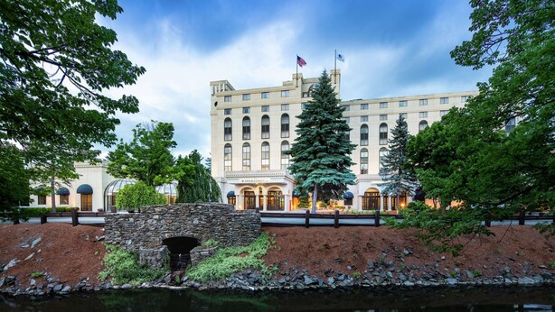 A large, historic building with a stone bridge over a reflective water body, surrounded by trees and a well-maintained garden. - DoubleTree by Hilton Nashua (Nashua)