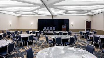 A conference room with round tables, chairs, and a stage with a podium.