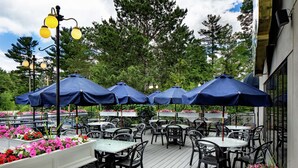 An outdoor patio with tables and chairs under blue umbrellas, surrounded by flower planters. - DoubleTree by Hilton Nashua (Nashua)