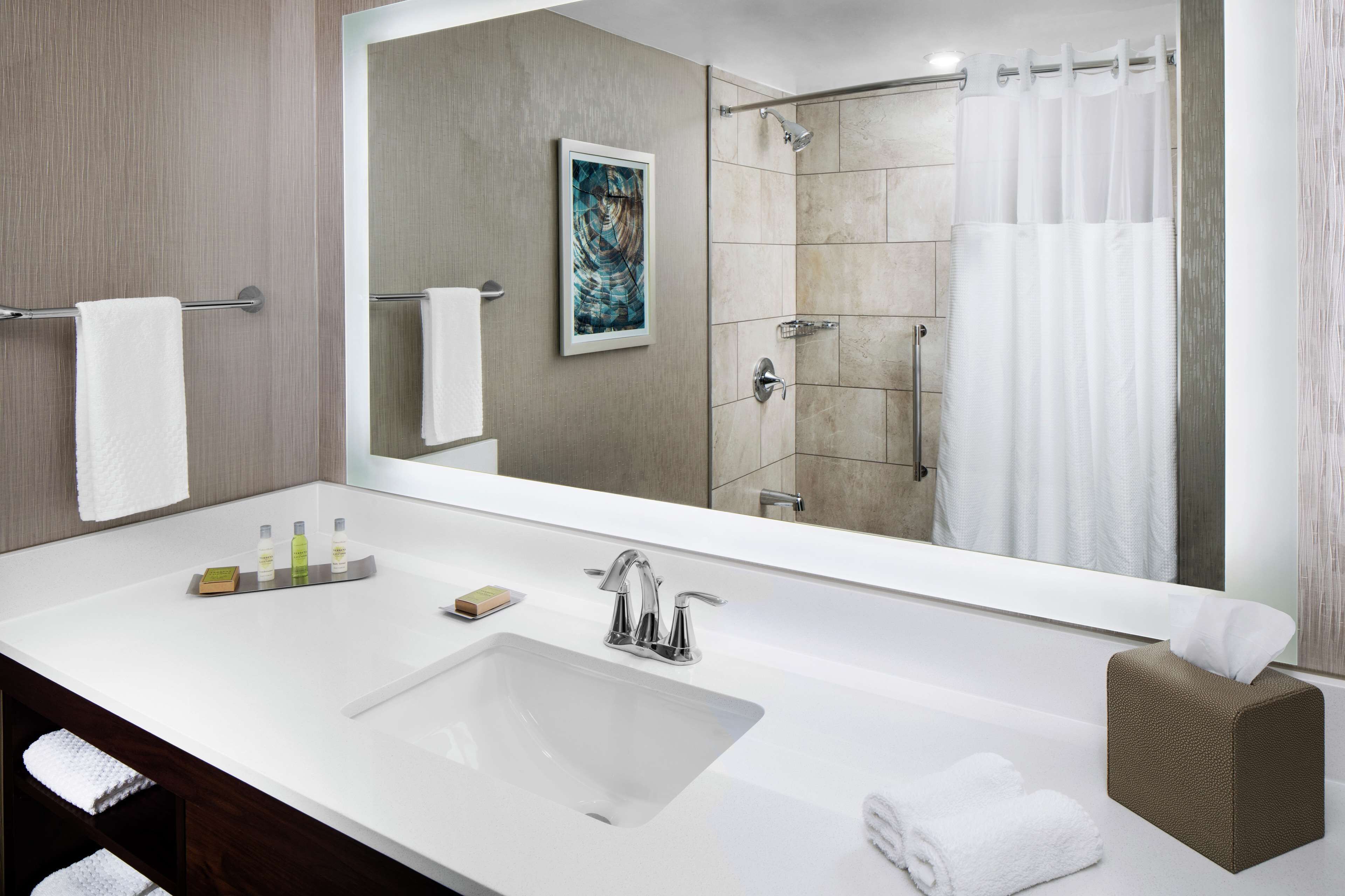 A modern bathroom with a large mirror, a white sink, a shower area, and a towel rack.
