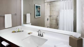 A modern bathroom with a large mirror, a white sink, a shower area, and a towel rack.