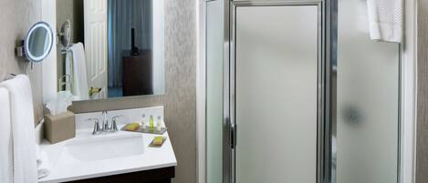 A bathroom with a glass shower enclosure, a sink with a mirror, and a towel rack.