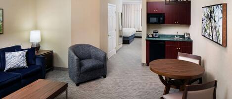 A hotel room with a sofa, armchair, dining table, and kitchenette.