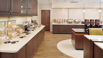 A hotel kitchen with a long counter, various food items, and coffee machines.