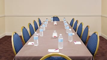 Une salle de conférence avec une longue table, des chaises bleues et des bouteilles d’eau.