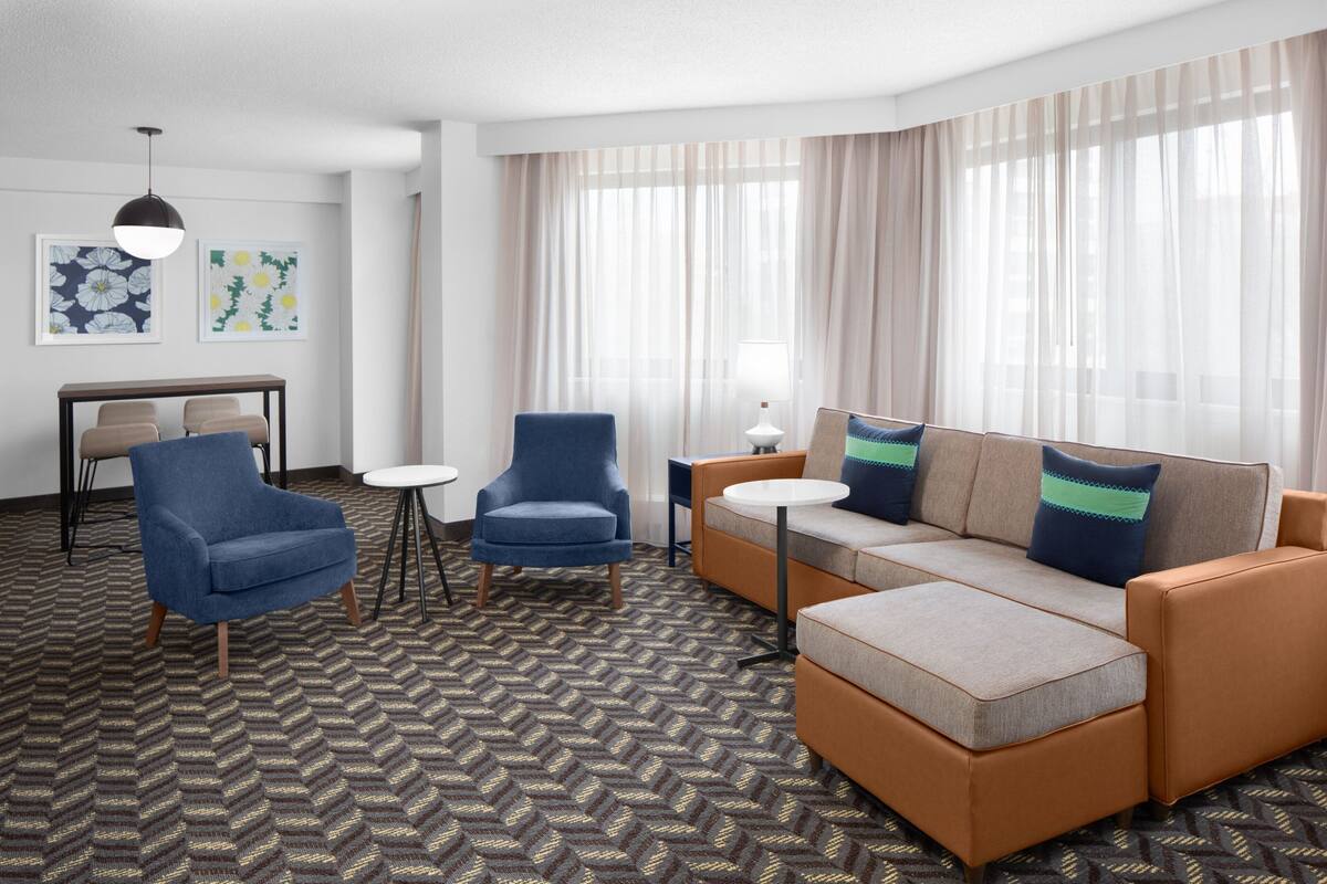 A hotel room with a sofa, two armchairs, a small table, and a lamp.