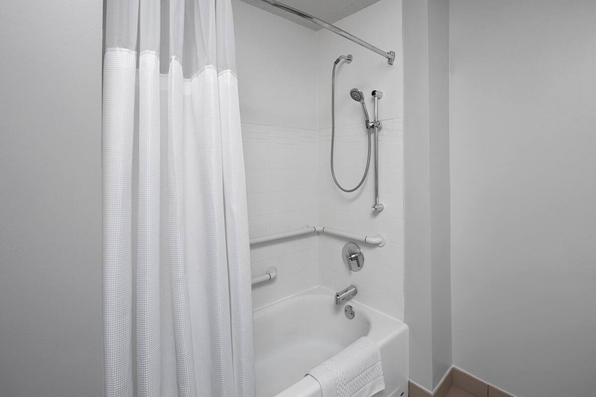 A bathroom with a bathtub, shower, and handrails.