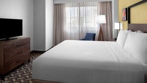 A hotel room with a large bed, a television on a wooden dresser, a desk with a lamp, and a window with curtains. - Residence Inn by Marriott White Plains Westchester County (White Plains)