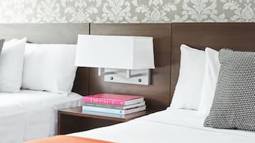 A hotel room with two beds, a nightstand with books, and a patterned wallpaper.