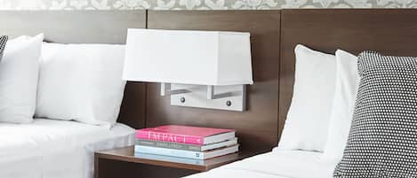 A hotel room with two beds, a nightstand with books, and a patterned wallpaper.