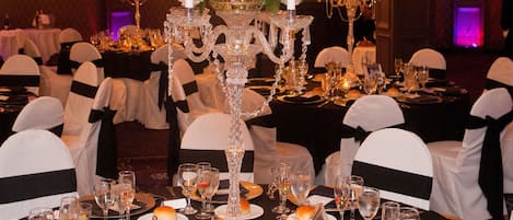A banquet hall with round tables set for a formal event, featuring crystal candelabras and floral centerpieces.