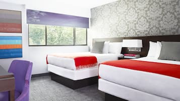 A hotel room with two beds, a desk, a purple chair, and a window with a view of trees.
