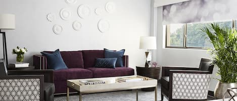 Una sala de estar moderna con un sofá morado, sillones estampados, una mesa de centro y decoración en la pared.