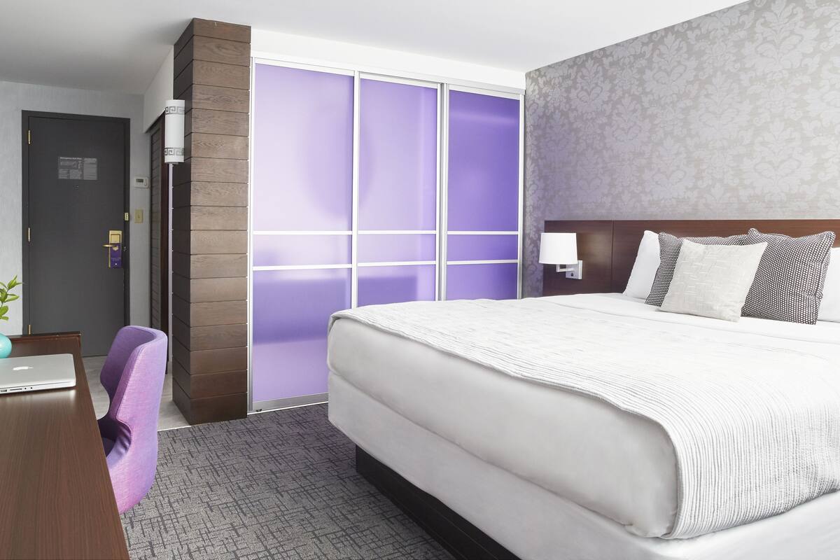 Habitación de hotel con cama, escritorio, silla y puerta corredera.