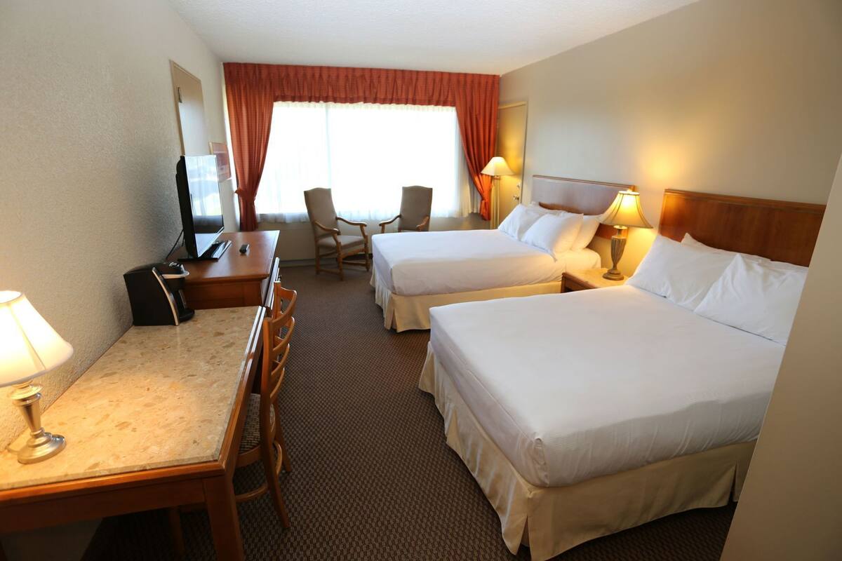A hotel room with two beds, a desk, a chair, a TV, and a window with curtains.