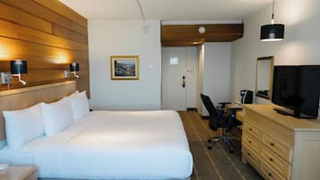 Habitación de hotel con una cama grande, un escritorio con silla, cómoda, televisor y dos lámparas de pared.