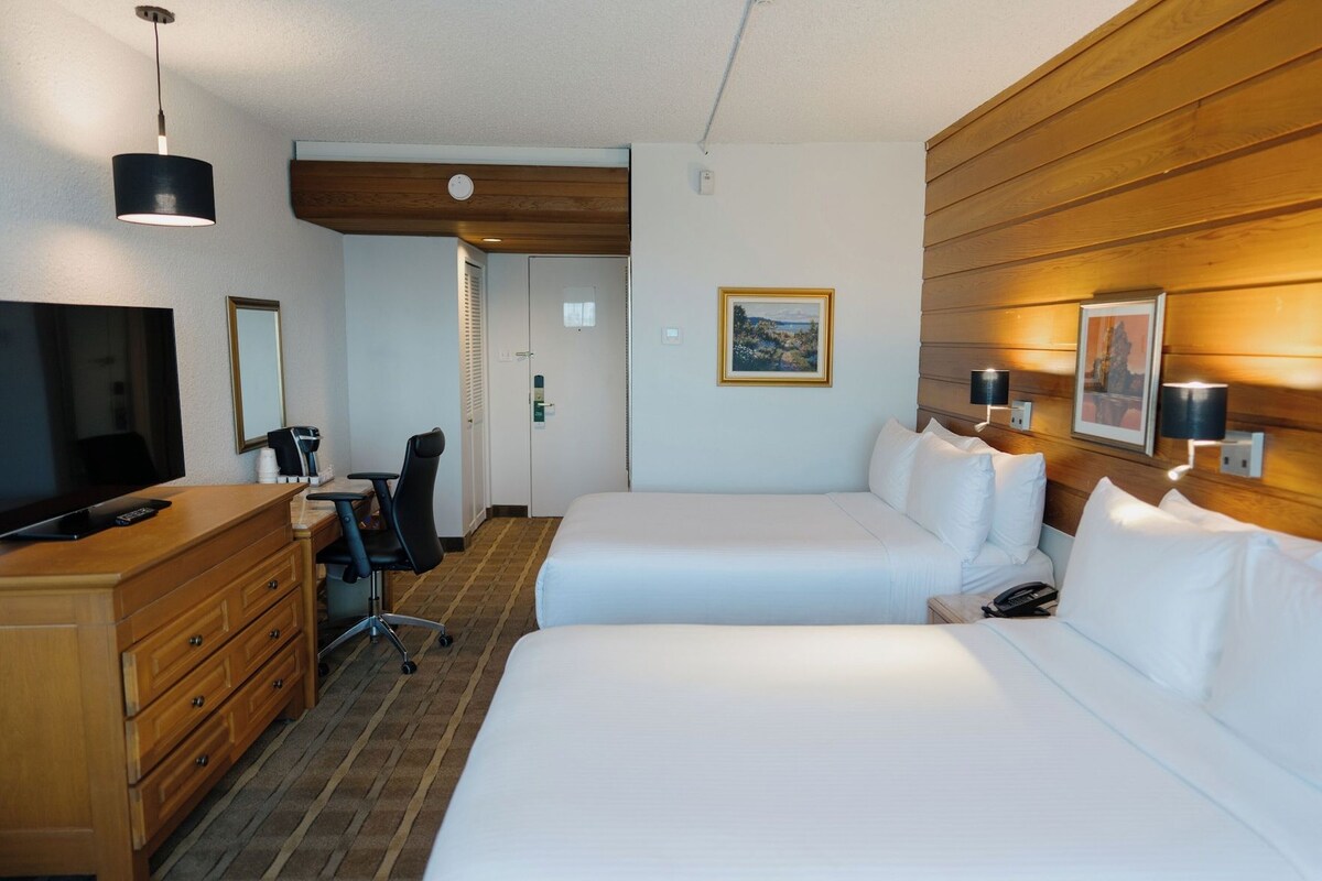 Habitación de hotel con dos camas, un escritorio, una silla, un televisor y un panel de pared de madera.