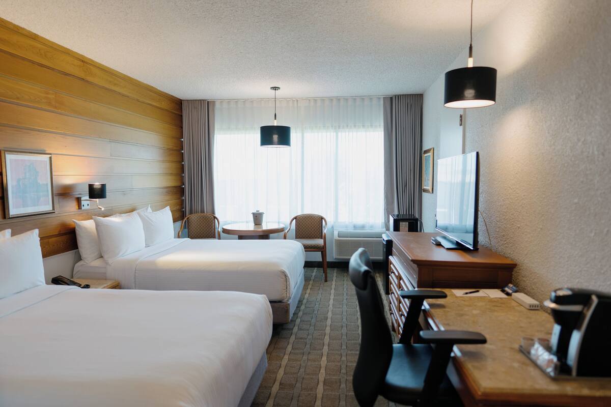 A hotel room with two beds, a desk with a chair, a television, and a window with curtains.