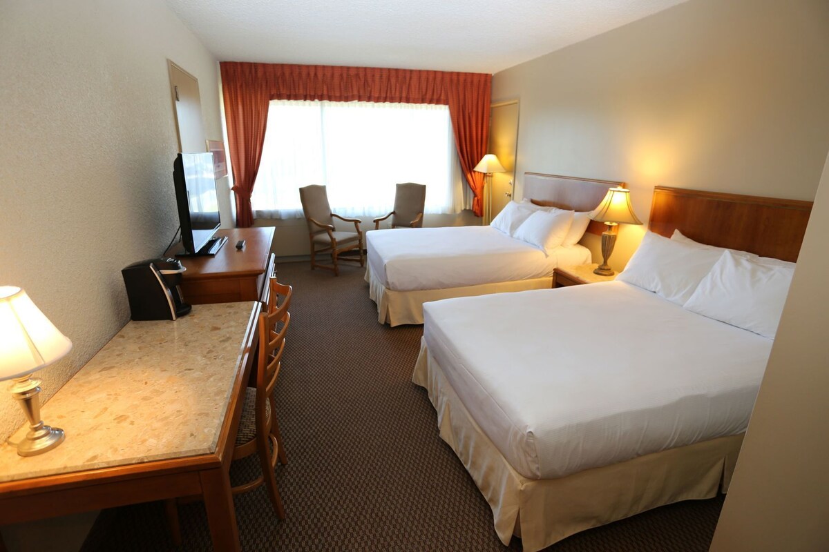A hotel room with two beds, a desk, a chair, a TV, and a window with curtains.
