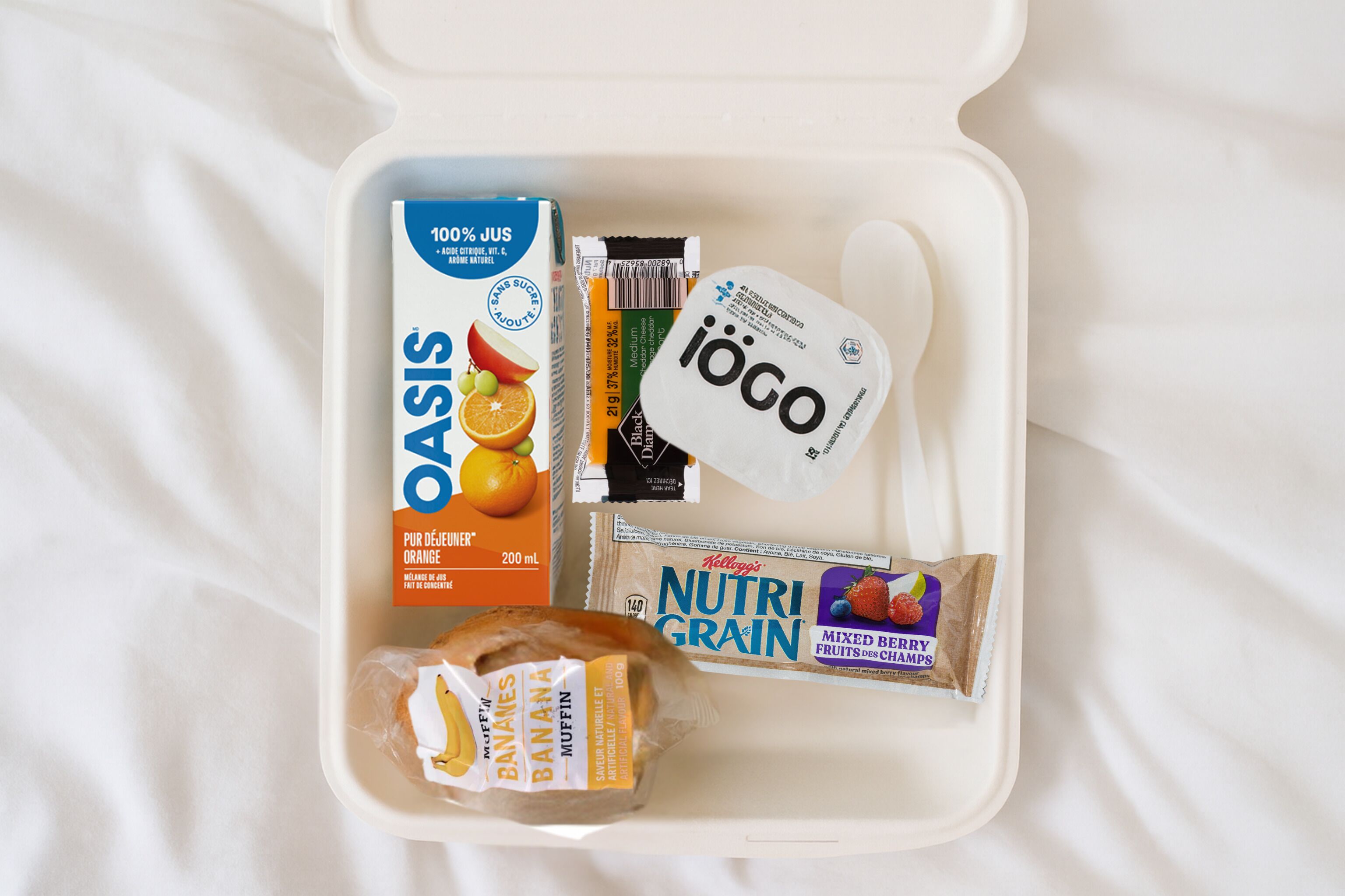 A meal kit with a box of OASIS orange juice, a bag of Ioco chocolate, a Nutri Grain mixed berry snack, and a banana muffin.