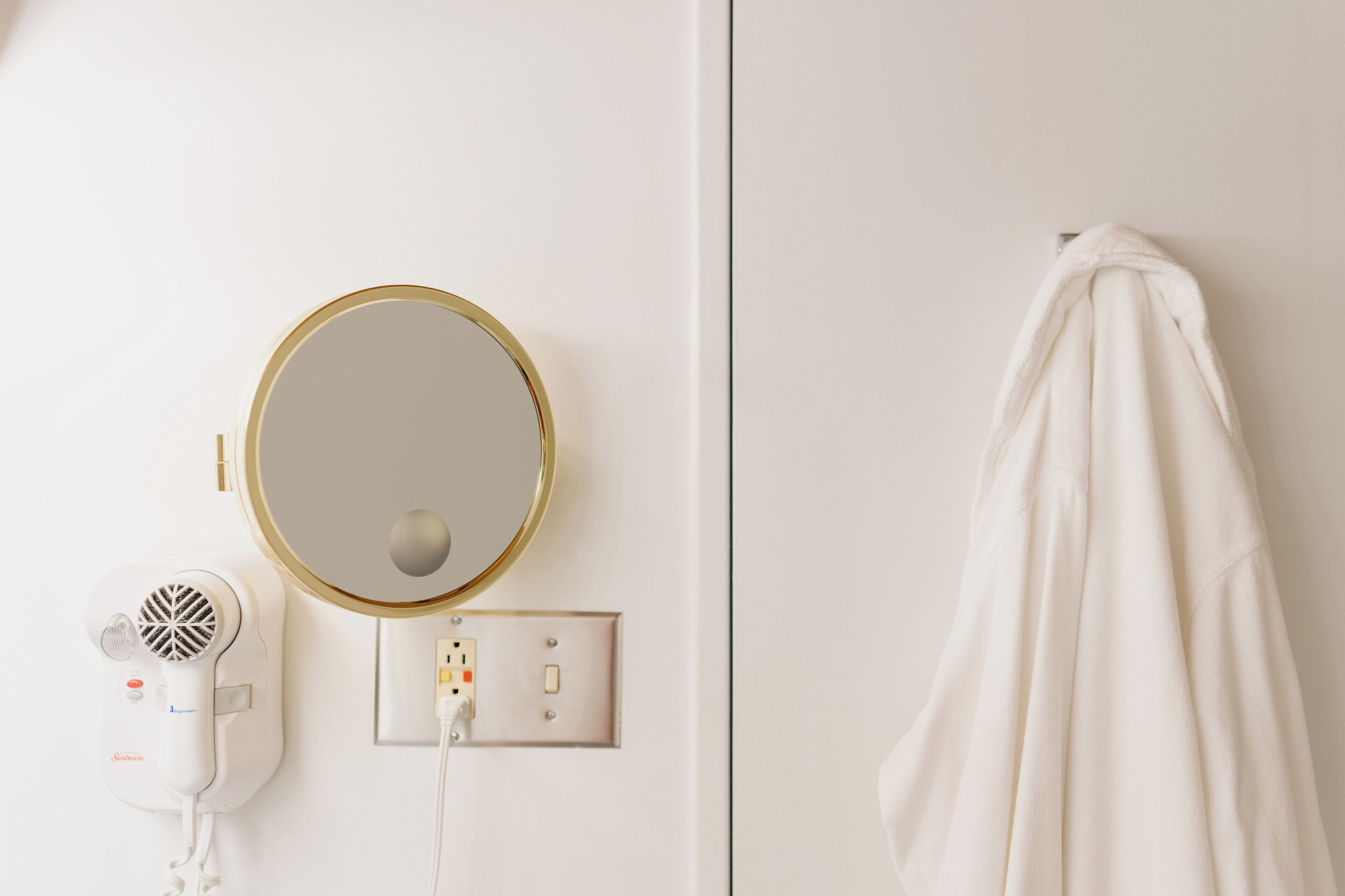 A bathroom with a hairdryer, a round mirror, and a towel hanging on the wall.