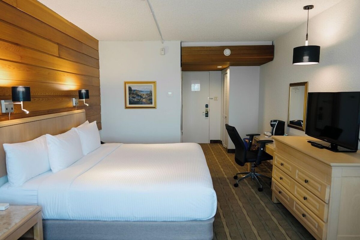 Una habitación de hotel con cama, escritorio con silla, televisión y cómoda.