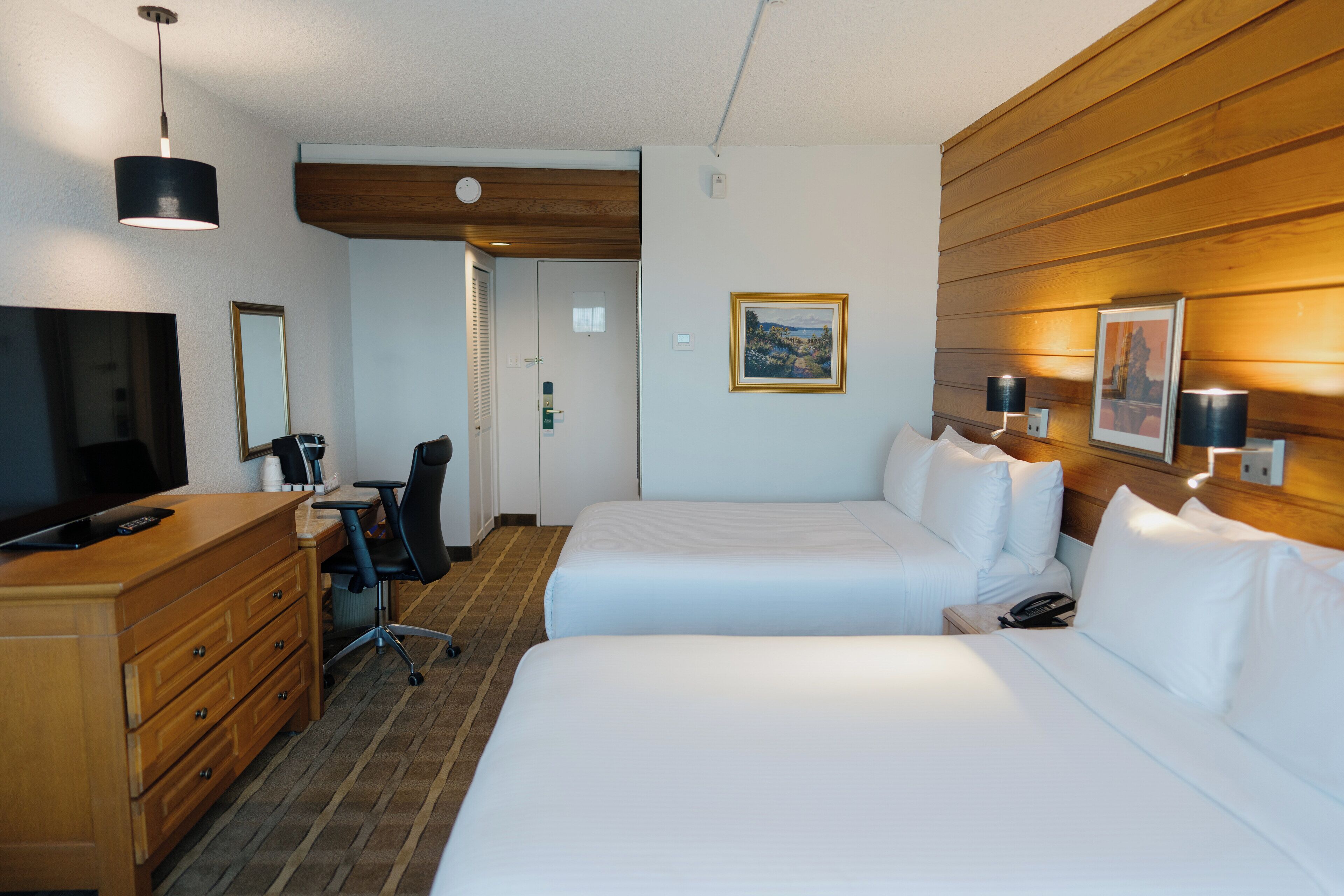 Habitación de hotel con dos camas, un escritorio, una silla, un televisor y un panel de pared de madera.