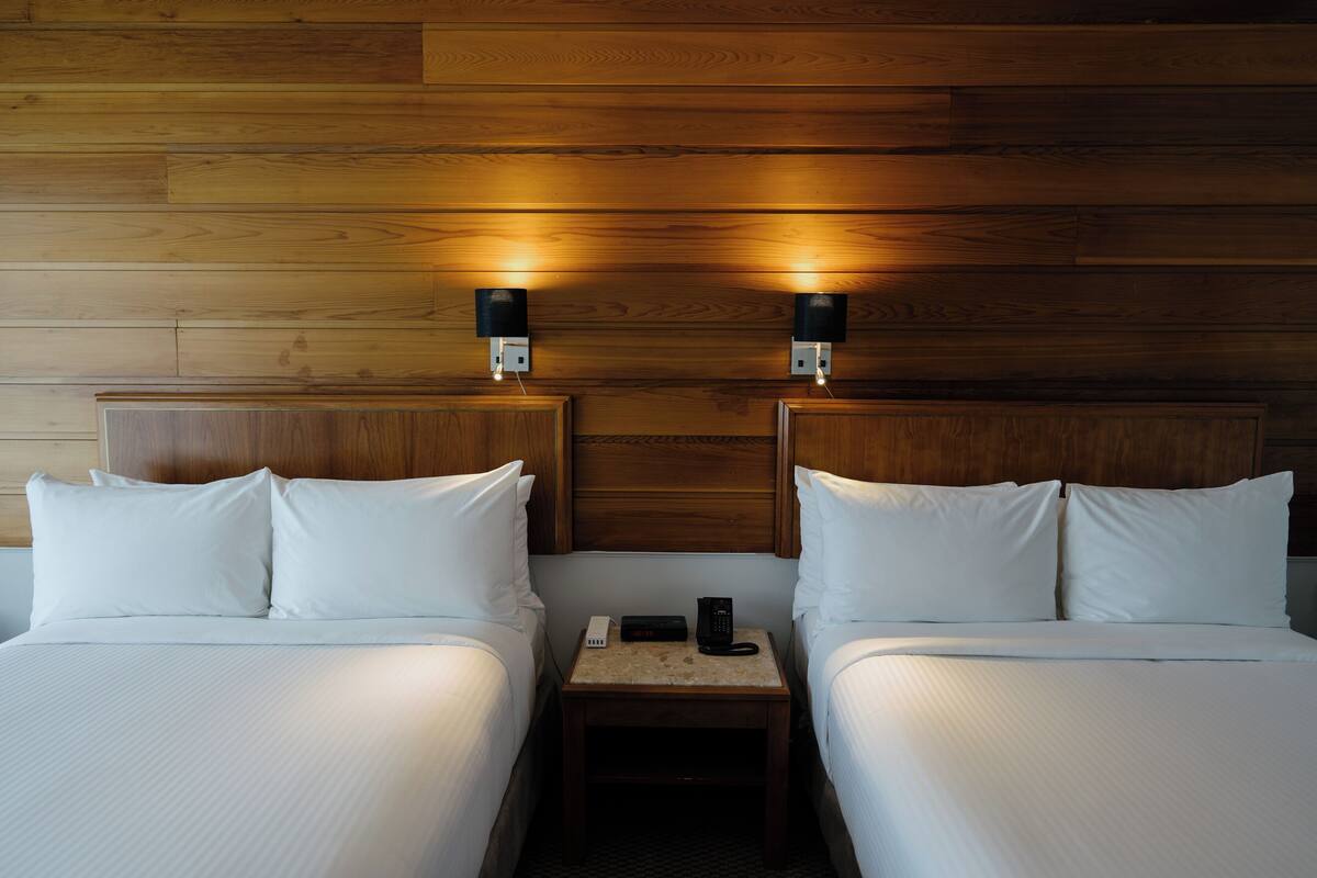 A hotel room with two beds, wooden headboards, and bedside lamps.